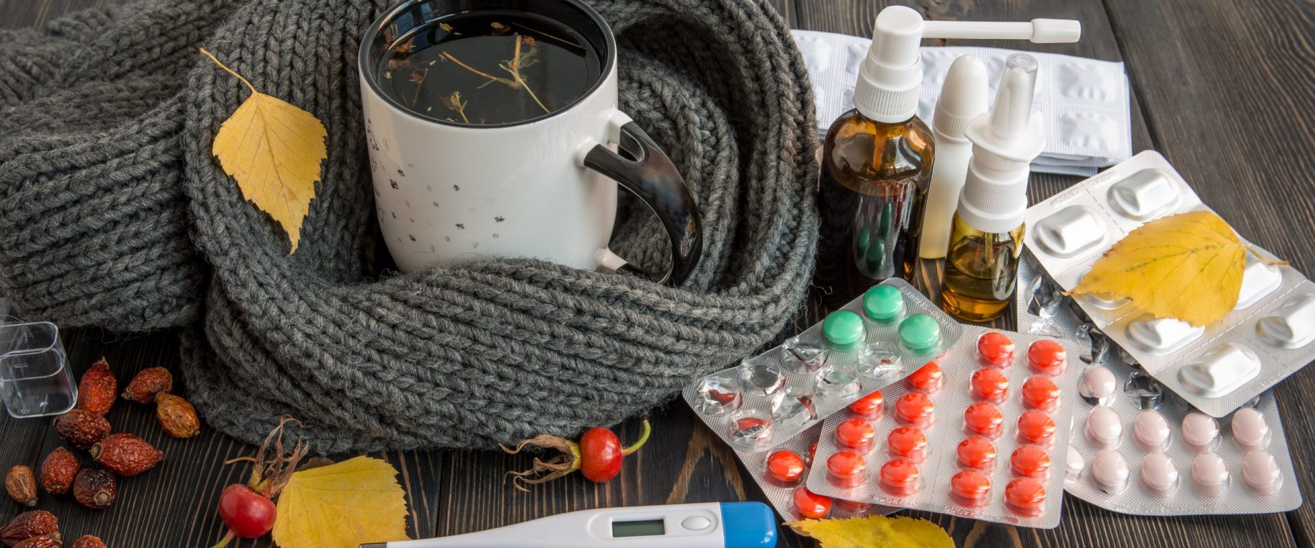 Pills, nose drops and hot tea with lemon for colds, treatment of , flu runny Mug with herbal tea and cold, flu medicine on a wooden table. The thermometer with high temperature. Fall leaves